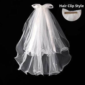 Close-up of white bridal veil with satin bow, pearls and metal hair clip detail