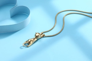 Detail of a golden cat pendant on a box chain over a blue background with paper hearts