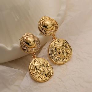 Macro detail of gold-plated geometric earrings with embossed disc and woven texture