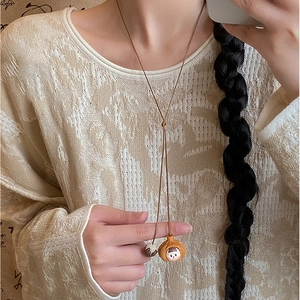 Girl character pendant on a long brown wax cord necklace worn over a white knit sweater