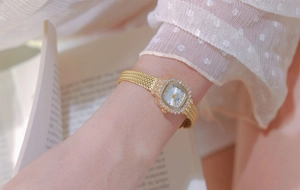 Close-up of gold ladies square watch with rhinestone bezel on woven mesh strap