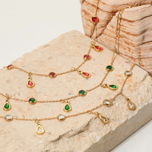 Multi-layer gold tassel anklet with red green white zircon charms on stone background