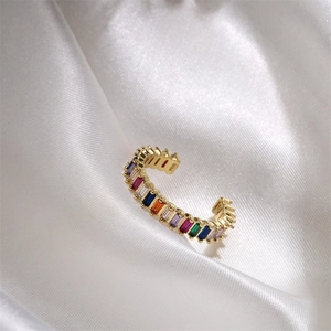 Detail view of gold ring with multicolor rectangular zircon inlays on white silk background