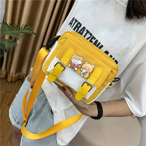Detail of yellow and white canvas crossbody bag with adjustable strap and cute charms