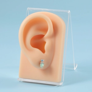 Detail shot of heart and round light green and blue zircon studs on a silicone ear model