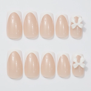 French tip press-on nails in nude pink with 3D white bow accents and glossy finish