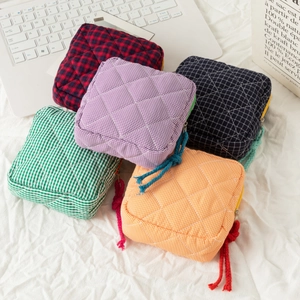 Detailed stack of five colorful quilted checkered cosmetic bags on a white fabric surface