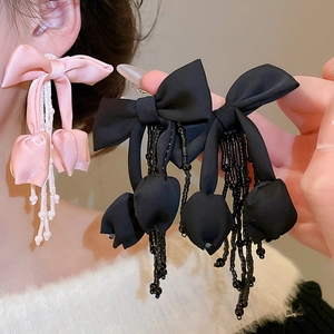 Close-up of bow knot fabric earrings with crystal fringe in pink and black colors