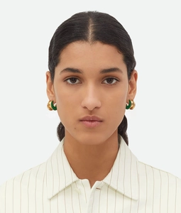 Front close-up of a model wearing gold C-shaped earrings with green enamel inlay