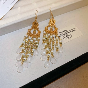 Detail of bohemian gold drop earrings featuring white beads and elegant tassel pendants