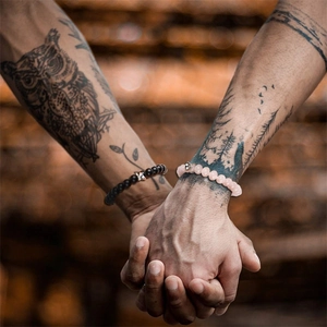Close-up of black matte and pink stone bead bracelets worn by a couple holding hands