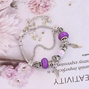Detailed view of silver snake chain bracelet with purple glass beads and angel wing charms