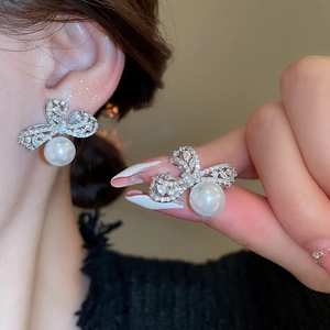 Close-up of bow earrings with zircon pavé and white pearls on model and held in hand