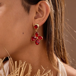 Close-up of a gold flower earring with five red gemstones worn on a model's ear
