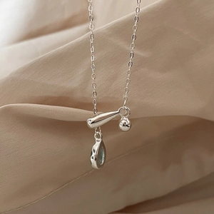 Macro shot of silver teardrop necklace featuring light blue stone and bar pendant details