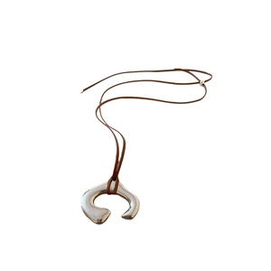 Modern irregular C-shaped silver pendant necklace with brown cord on white background