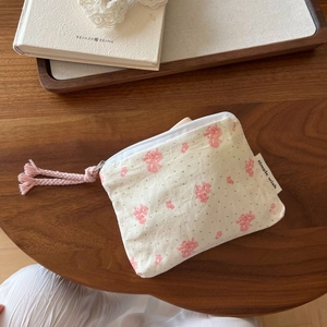 Floral cotton pouch close-up with pink woven zipper pull on a vintage wooden table