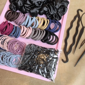 Flat lay of diverse hair accessories set on a pink tray including scrunchies and ties