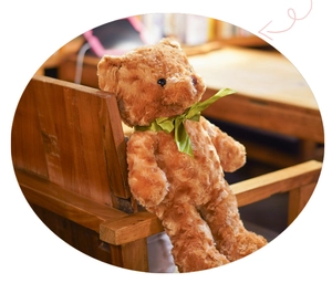 Detailed close-up of a curly brown plush teddy bear decorated with a green satin ribbon bow tie
