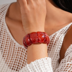Detail shot of red glitter acrylic segments on elastic bracelet worn with white knitwear