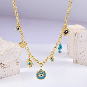 Detail of gold necklace with evil eye, sun, and heart charms on a white stone background