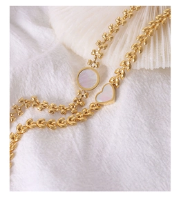 Macro shot of 18K gold wheat chain bracelet with heart shell and round mop charms