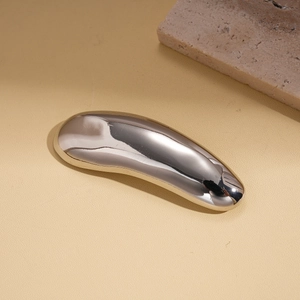 Close-up of polished silver teardrop brooch on a warm textured surface with stone accent