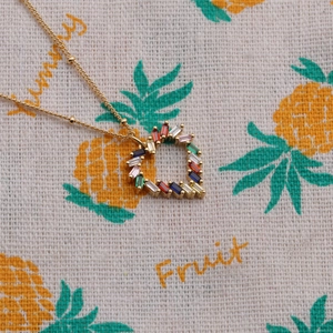 Macro shot of gold heart necklace featuring colorful baguette zirconia on pineapple cloth