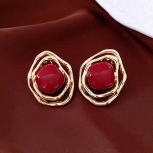 Macro detail of golden irregular hollow earrings with a polished red square stone center