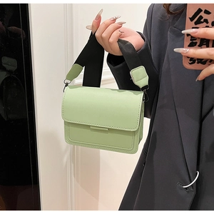 Close-up of light green crossbody square bag with a wide black woven shoulder strap