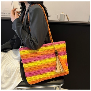 Close-up of woven straw tote bag featuring colorful gradient stripes and tassel bead detail