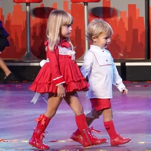 Children in red festive holiday outfits with knee-high pompom socks on a fashion runway