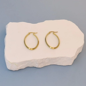 Close-up of gold oval hoop earrings with flat surface texture on white stone