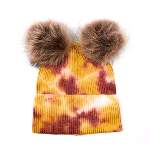 Détail d'un bonnet en tricot tie-dye jaune et rouge avec deux grands pompons marrons