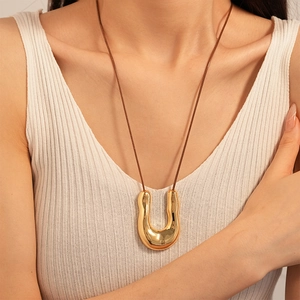 Close-up of golden liquid metal U-shaped pendant on a brown cord necklace for women