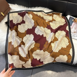 Detailed view of square silk scarf with floral print on plush background with accessories