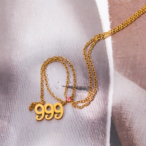 Close-up of golden double-layer necklace with 999 number pendant and pink gemstone detail