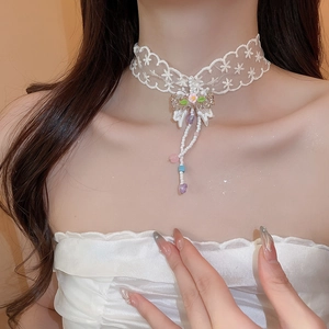 Detail of white lace choker with bow, pink floral accent and colorful hanging tassels
