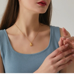Detail of 3D bear pendant necklace in gold finish on female model with blue top