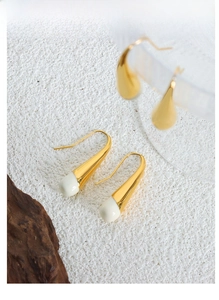 Detail of French style gold-plated earrings with white teardrop resin on a textured surface