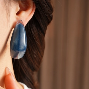 Close-up of a blue resin waterdrop earring featuring a marble texture on model ear