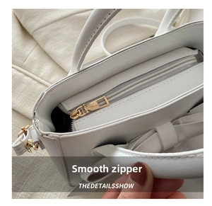 Close-up of a smooth gold metal zipper closure on a white leather handbag detail