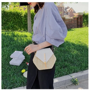 Outdoor shot of a woven hexagonal crossbody bag with white leather flap and chain strap