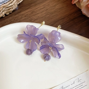 Detail of purple resin flower earrings with gold metal and zircon on white plate
