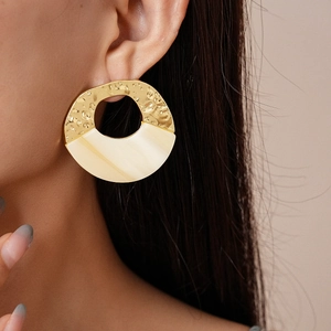 Close-up of geometric gold hammered earrings with cream white enamel inlay on model