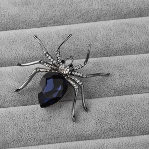 Macro detail of a blue teardrop gemstone spider brooch with white rhinestone accents