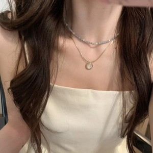 Double-layered gold necklace with blue beads and round opal pendant on a model