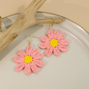 Gros plan de boucles d'oreilles marguerites roses tissées main sur plateau en céramique