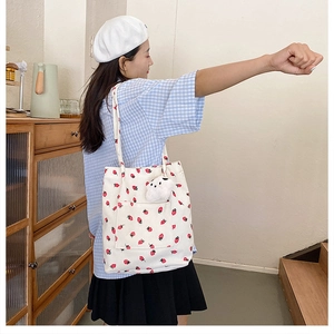 Detail of off-white corduroy tote bag with red strawberry prints and a plush pendant