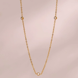 Detail of a thin gold chain necklace with three round micro-pave crystals on pink background